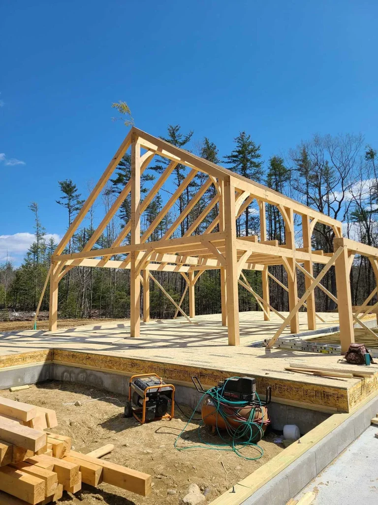 Timber frame bents raised on a new foundation with timbers stacked nearby