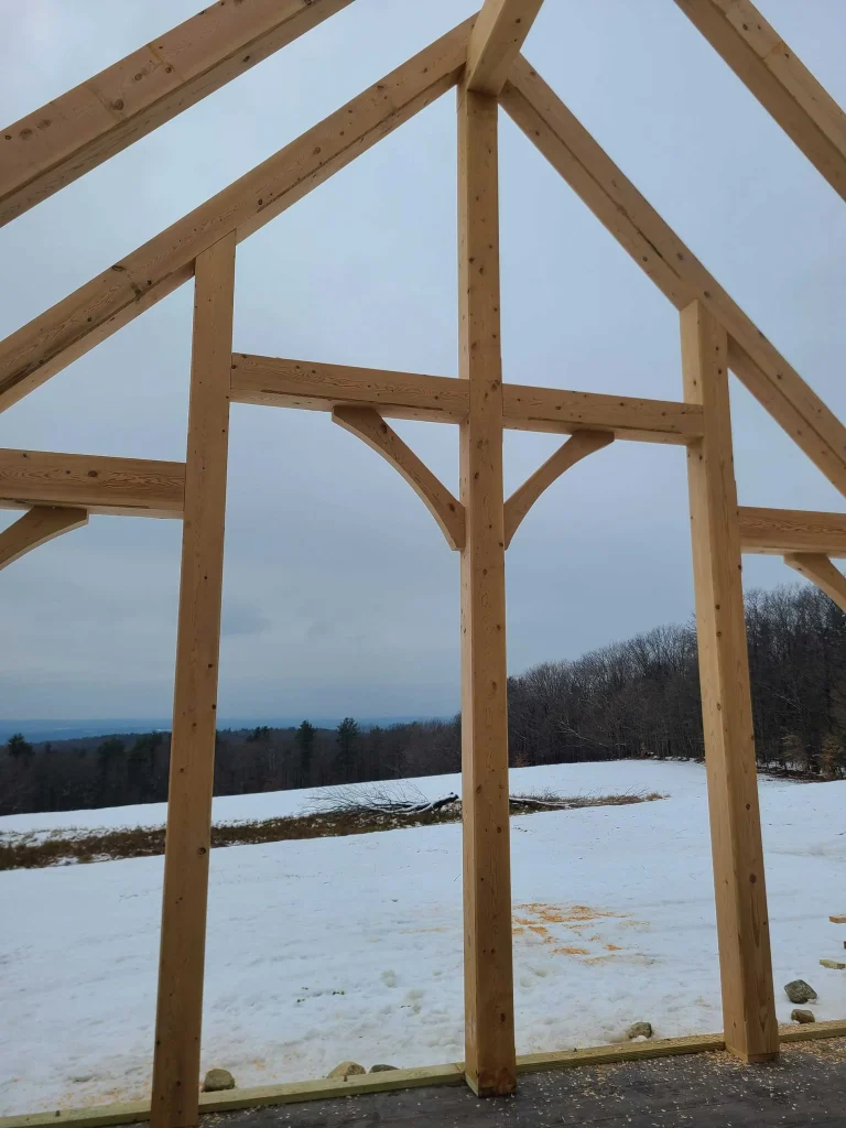 Timber frame gable end with king post and braces overlooking a snowy field