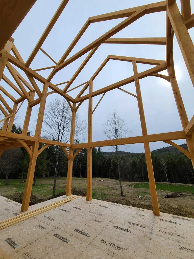 Timber frame bents and braces raised on a subfloor overlooking a field