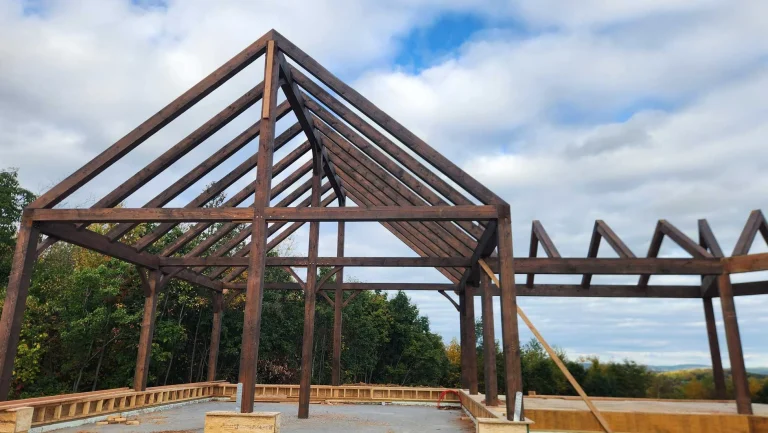 Dark-stained timber frame pavilion with exposed rafters on a stone base