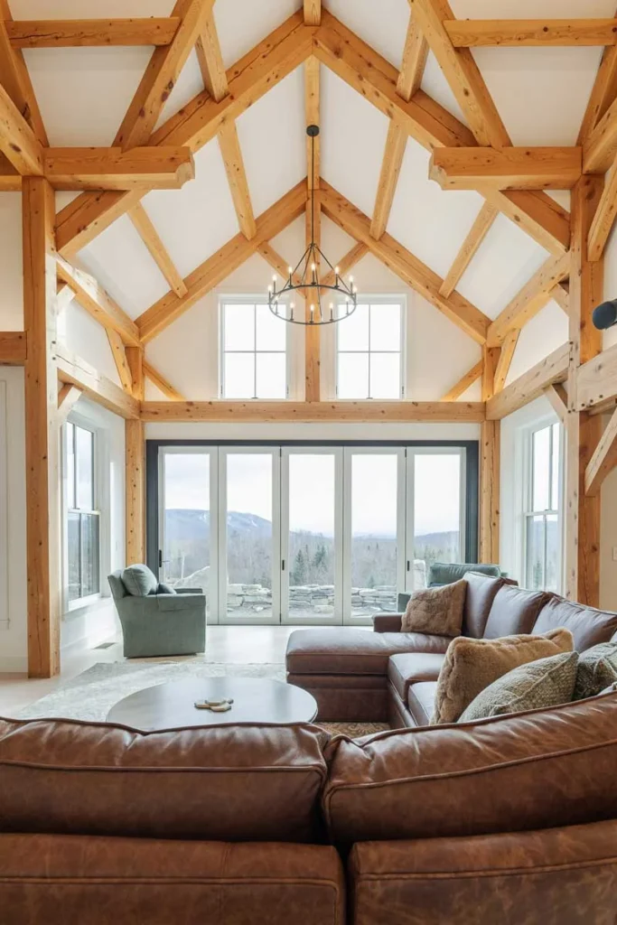 Vaulted timber frame great room with trusses, iron chandelier and tall windows