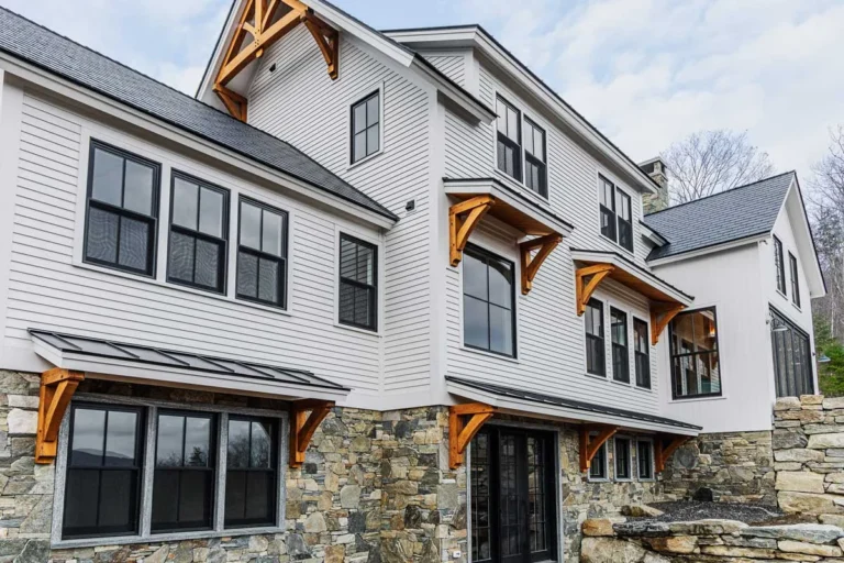 White farmhouse with timber frame gable trusses and window brackets on stone base