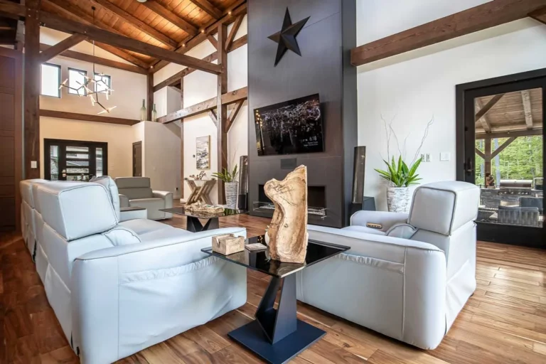 Timber frame great room with exposed beams, black stone fireplace wall and white leather seating